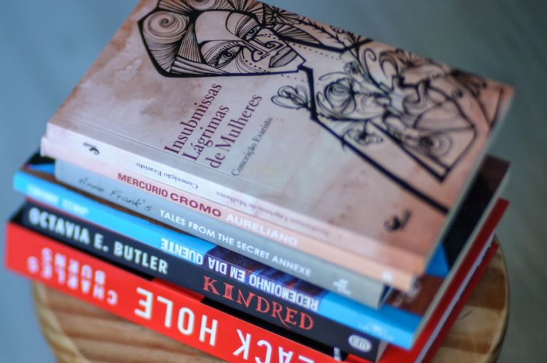 a stack of books sitting on top of a wooden table — Foto por Mayumi Maciel na Unsplash